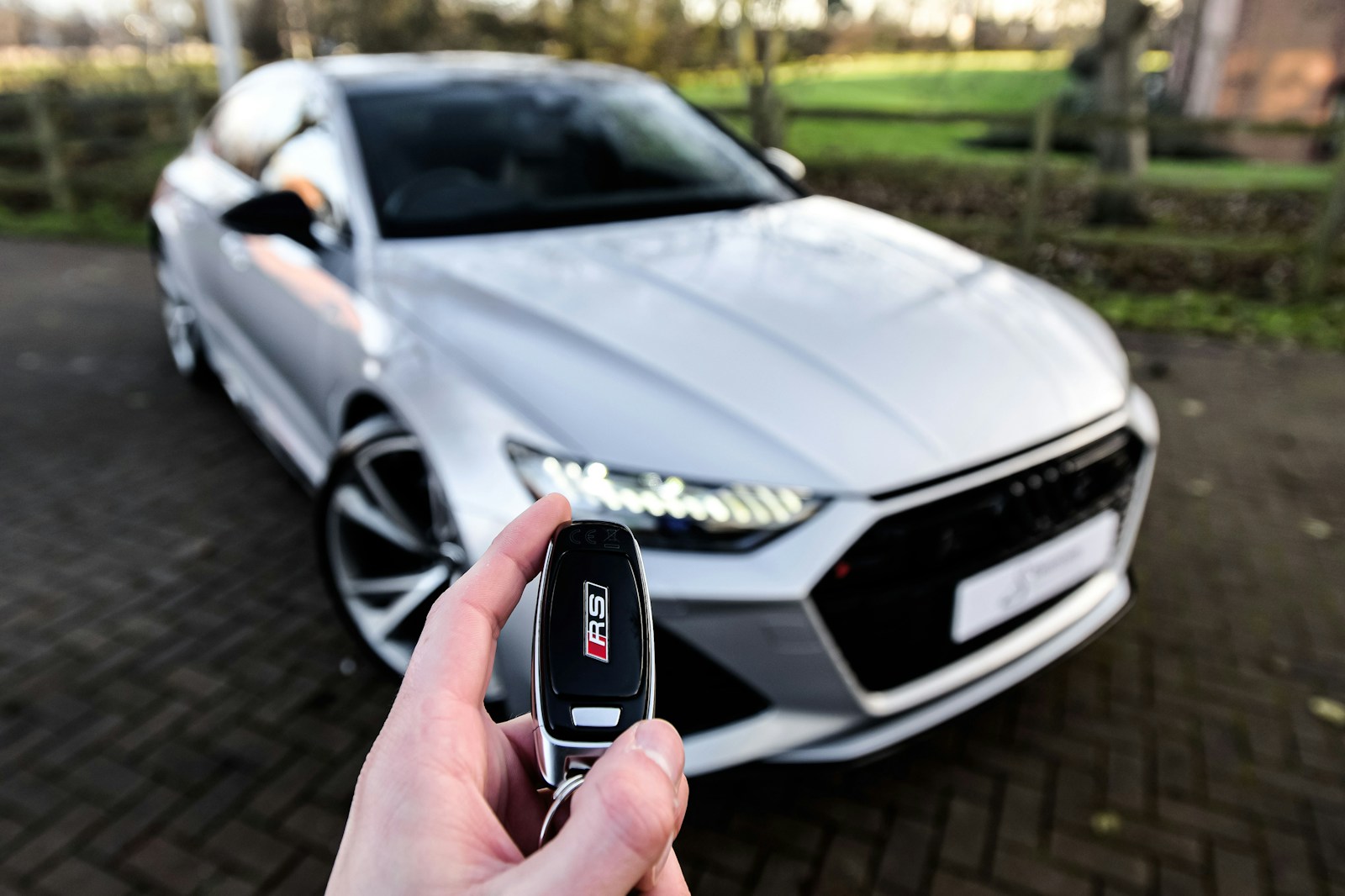 a person holding a car key in front of a silver car because he is buying a new car